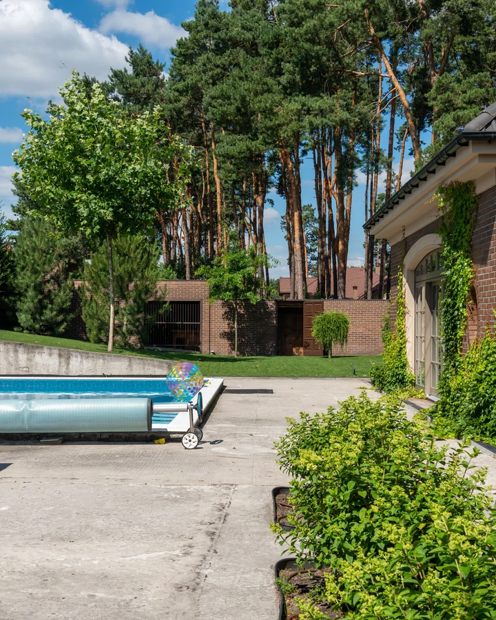 Concrete pool deck around a covered backyard pool beside a brick pool house