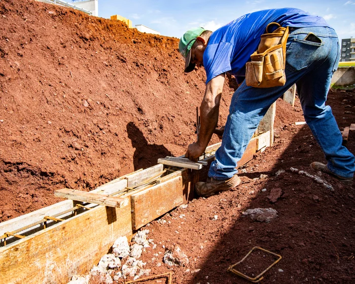 Worker setting wood forms for a concrete footing in a dug trench